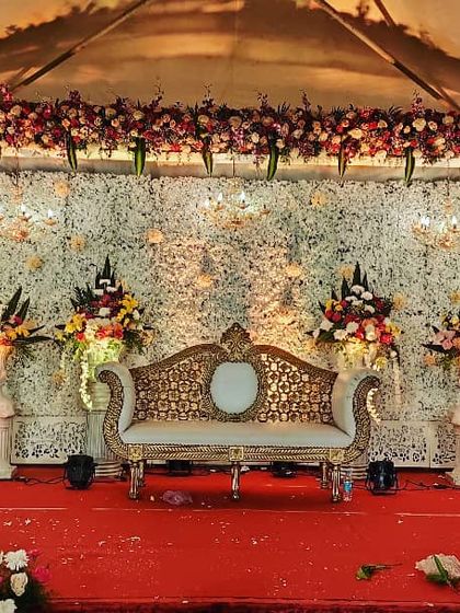 A classic wedding stage with a backdrop of white flowers and elegant gold-and-cream seating, ready for the main event.