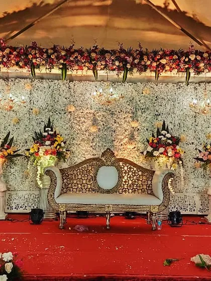 A classic wedding stage with a backdrop of white flowers and elegant gold-and-cream seating, ready for the main event.