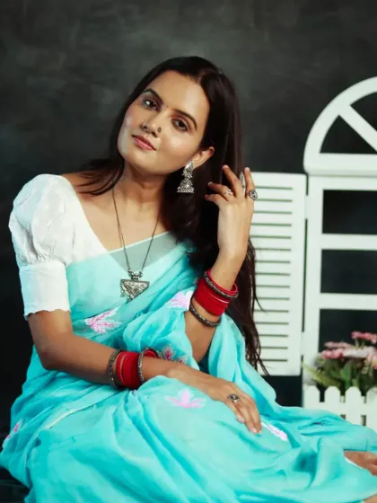 A full-length seated portrait showing the entire saree and the studio setup. The white window prop adds a touch of charm to the scene.