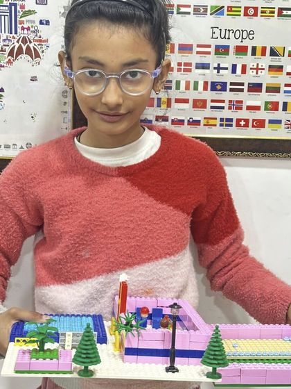 A girl proudly presents her LEGO creation, a pink and white structure with a swimming pool area.