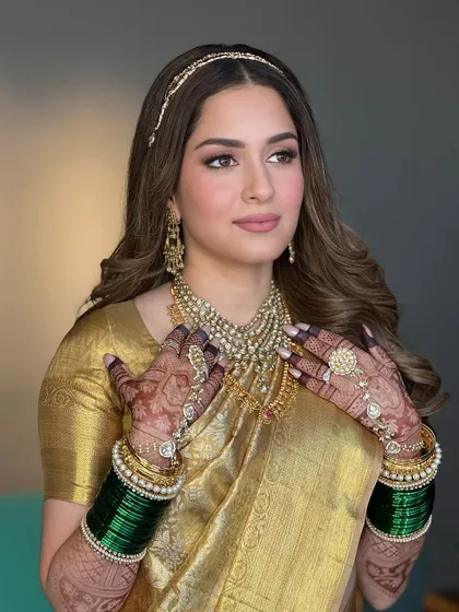 A beautiful close up showing the bride's hands framing her face. This highlights the harmony between the golden saree, the traditional jewelry, and the warm, radiant makeup.