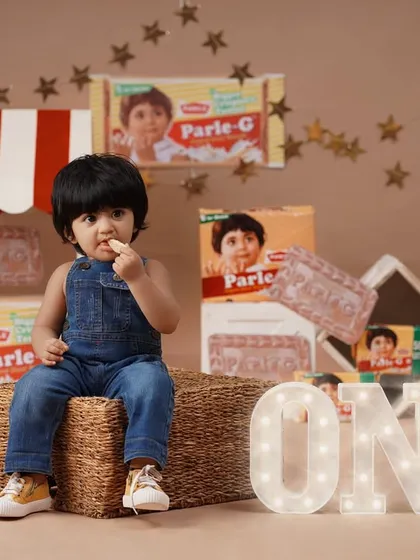 The Parle-G theme is combined with a first birthday milestone, featuring a light-up 'ONE' sign next to the baby girl.