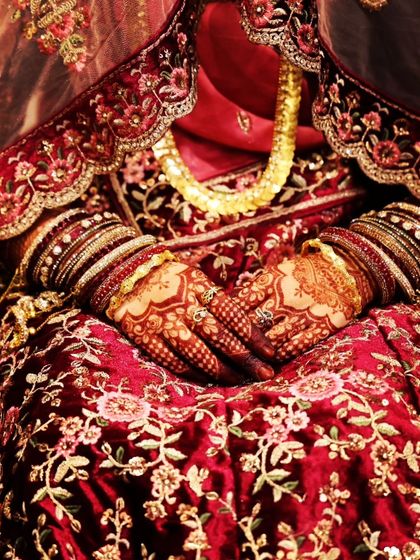 The perfect shot of a bride's hands, showcasing the deep, rich henna stain against her magnificent red bridal lehenga.