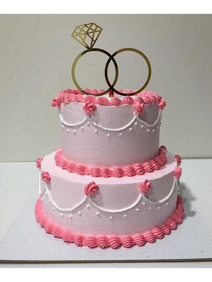 A classic two-tier engagement cake in a lovely pink shade. The vintage piping details and ring topper make it a timeless and elegant choice for celebrating your special day.