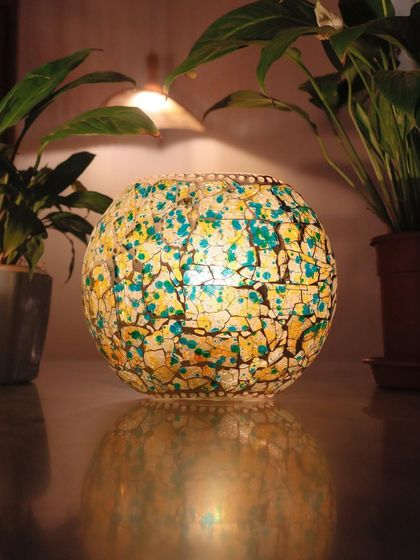 A handcrafted mosaic lamp that creates a warm, inviting glow. The intricate crackled glass texture in shades of yellow and teal makes this more than just a light source; it's a decorative vibe.