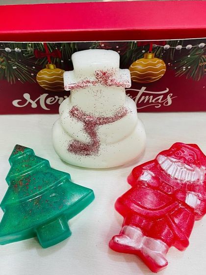 A trio of festive Christmas-themed soaps. This set includes a sparkly snowman, a glittery Christmas tree, and a red Santa Claus soap, ready to be gifted.