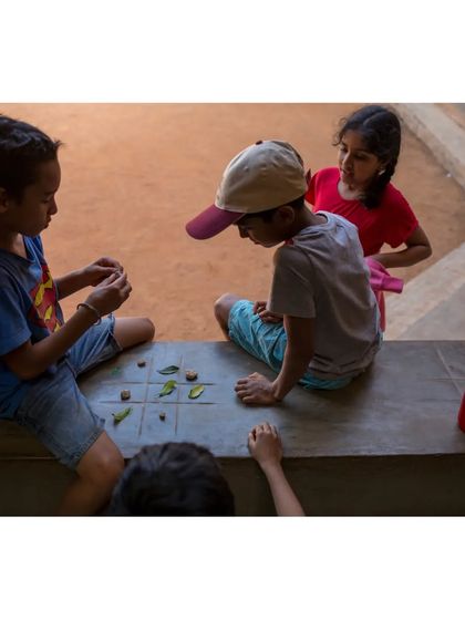 Children playing a game with leaves and stones on a built-in seat at Buddhi School. Our designs often include informal spaces that encourage spontaneous interaction, play, and connection with nature.