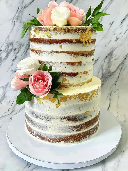 I love the rustic yet chic look of a semi-naked cake. This two-tier version allows the natural cake layers to peek through a light coating of buttercream, decorated with fresh pink and white roses and flecks of edible gold leaf for a touch of elegance.