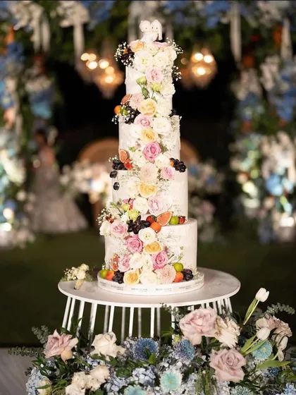 A stunning multi-tiered wedding cake adorned with fresh flowers and fruits, serving as both a dessert and a beautiful decor piece.