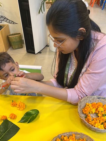 An educator provides gentle support as a child learns to string flowers. This co-regulation helps the child build confidence and persist through a challenging task, turning potential frustration into a moment of connection and achievement.