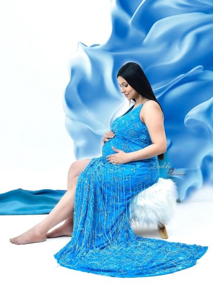 A serene portrait of a mom-to-be in a sparkling blue gown. The flowing blue fabric in the background adds a touch of magic and movement to this beautiful studio shot.