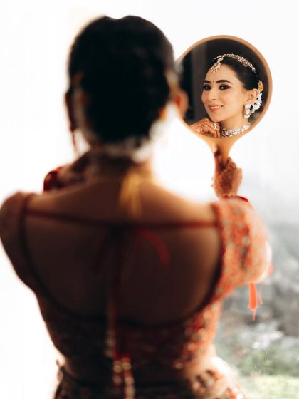A beautiful over-the-shoulder shot of the bride looking at her reflection. This captures a moment of self-reflection and happiness before the ceremony.