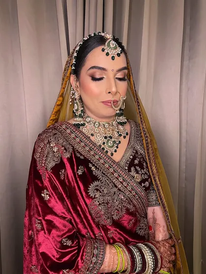 A bride adorned in sunset hues. This look showcases the art of enhancing beauty, with a focus on creating a warm, glowing look that complements the rich velvet of her outfit.