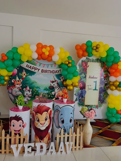 A classic jungle book style setup for a first birthday. It includes a circular backdrop with cartoon animals, character-themed pedestals, and a colorful balloon arch.