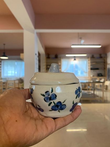 A student's hand-painted jar with a blueberry design. The simple, charming artwork and handmade form make this a truly special piece.