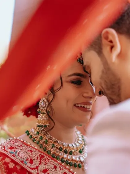 A romantic close-up of the couple under the bride's red veil, creating an intimate and colorful frame.