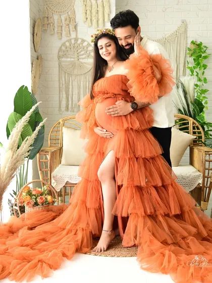 A stunning maternity portrait featuring a tiered, off-shoulder tulle gown in a bold orange. This photo, taken in our boho-chic studio set, showcases how we use fashion and texture to create high-impact, magazine-worthy images.