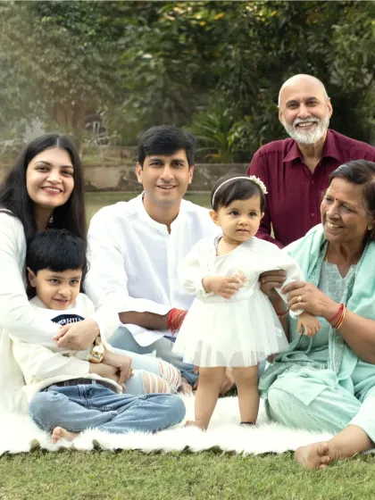 A beautiful multi-generational family portrait taken outdoors, featuring grandparents, parents, and children all smiling together on a sunny day.
