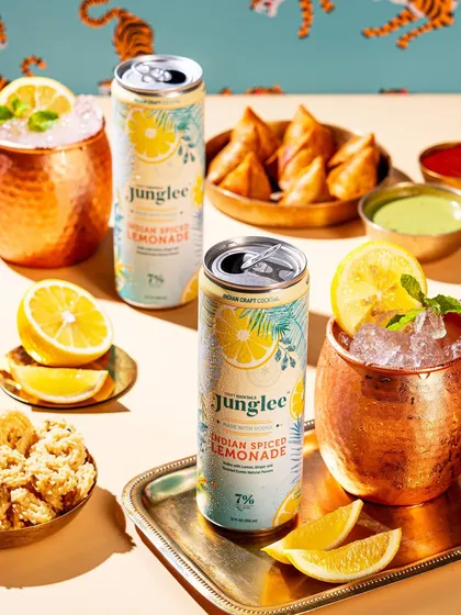 An elegant pairing of Junglee cocktails with Indian snacks like samosas. The use of copper mugs and a brass tray adds a touch of sophistication to the scene.