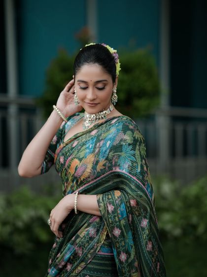 A serene and graceful portrait, focusing on the elegant posture and the fine details of the saree and jewelry. The soft outdoor lighting enhances the peaceful mood.