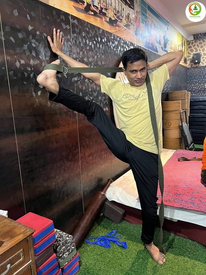 Practice makes progress. Here, a student uses the wall and a belt to deepen his stretch in Trivikram Asana, improving his hip and hamstring flexibility over time.