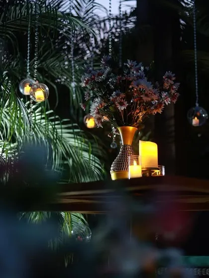 A close-up of the details. Hanging glass orbs with tea lights and a vase of flowers on the table add layers of elegance to this outdoor romantic dining experience.