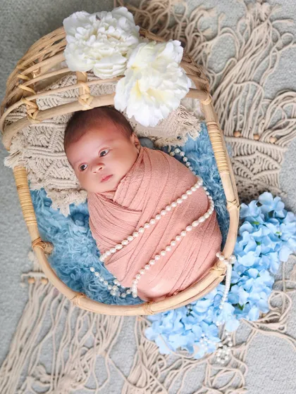 A side view of the baby in the cane bassinet, showing off the beautiful textures of the macrame blanket and floral accents.