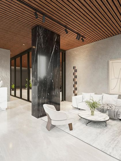 Inside the lobby, a comfortable waiting area is created with a plush white sofa and minimalist armchair. The space is defined by the contrast between the dark marble pillar, the light marble desk, and the warm wood-slatted ceiling.