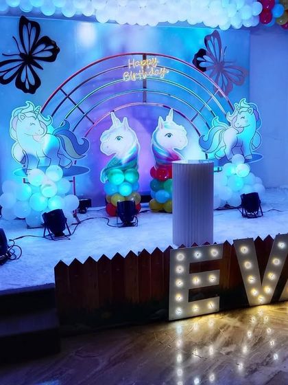 A magical unicorn theme for Eva's birthday. The stage features a rainbow arch, cute unicorn figures, butterfly details, and a light-up sign with her name, creating a dreamy and colorful setting.