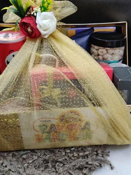 A large, beautifully wrapped Rakhi hamper in a golden basket, filled with snacks and chocolates.