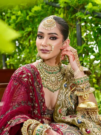 Adjusting her earring, this candid shot captures the bride's majestic presence. The heavy jewelry, from the maang tikka to the nath, is balanced with a strong yet elegant makeup look.
