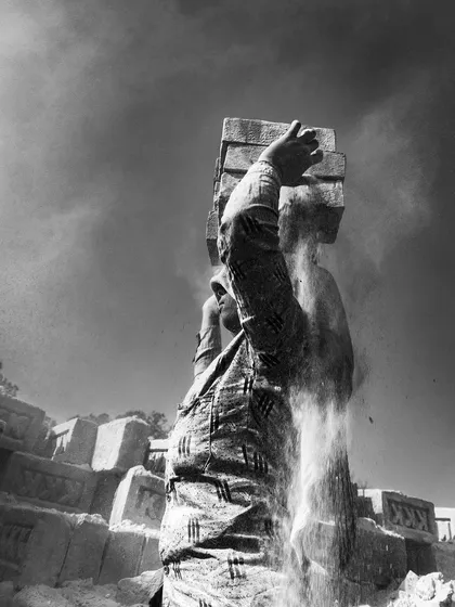 A low-angle black and white shot captures a worker lifting bricks, with dust cascading down, creating a dynamic and powerful image of labor.