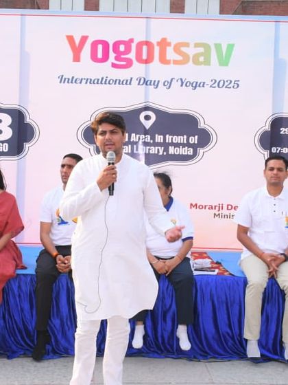 Addressing the audience during a large-scale yoga event. I focus on making yoga accessible and understandable for everyone, explaining the 'jeevan jeene ki kala' or the art of living, in a clear and engaging manner.