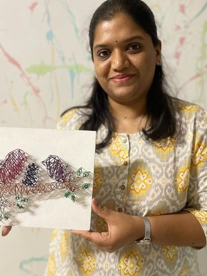A participant proudly holds her finished string art depicting a family of birds perched on a branch.