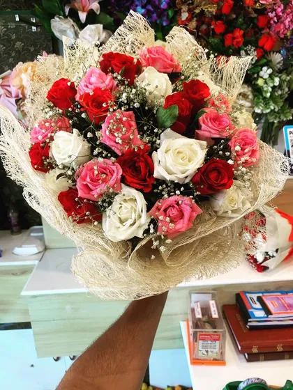 A beautiful bouquet of mixed red, pink, and white roses. The arrangement is wrapped in a natural jute net, giving it a rustic and organic feel.
