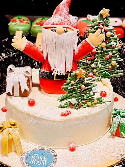 A festive Christmas cake featuring a hand-sculpted Santa Claus, a Christmas tree, and edible gift boxes. This cake brings the cheerful spirit of the holidays to your dessert table.