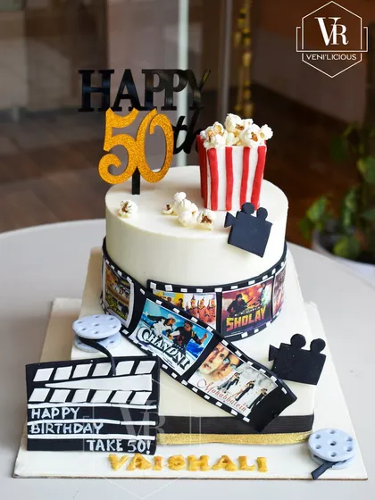 Take 50! This Bollywood-themed cake brings the drama of the silver screen to a 50th birthday party. It features an edible film strip with classic movie posters, a clapperboard, and a box of popcorn for a fun and nostalgic celebration.