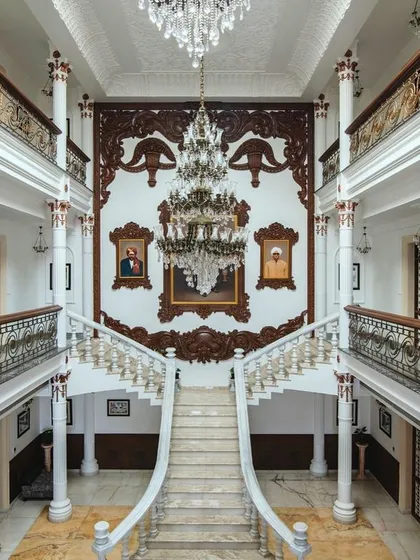 A direct, symmetrical shot of the grand staircase from an upper level, showcasing the intricate wooden carvings that frame the ancestral portraits.