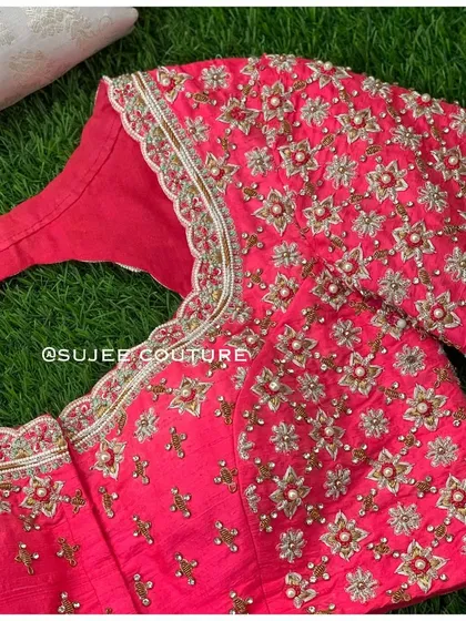 A close-up of the neckline and sleeve of the pink floral blouse. This view shows the detail of the star-shaped floral motifs created with zardozi and pearl centers.