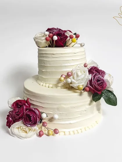An elegant two-tier cake with white buttercream and a cascade of red and white roses. This classic design is perfect for a wedding or a grand anniversary celebration.