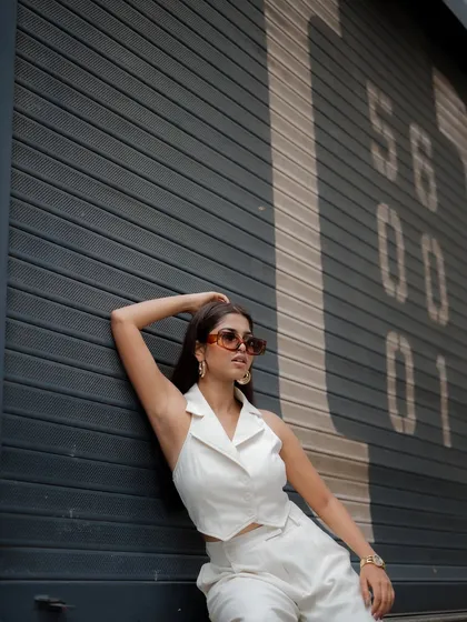 A profile shot of a model in a chic white outfit against a grey shuttered wall. The minimalist composition highlights her style and confidence.