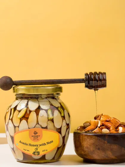 A jar of honey with nuts, with a honey dipper creating a perfect drip. This classic shot emphasizes the rich texture and quality of the honey.