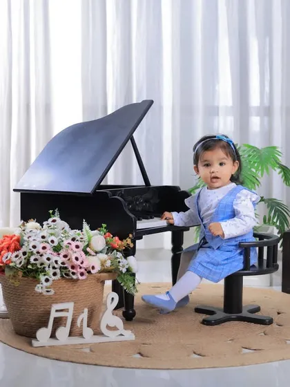 Looking right at the camera, this one-year-old is the star of her birthday photoshoot. The "ONE" blocks and piano prop create a perfect setting.