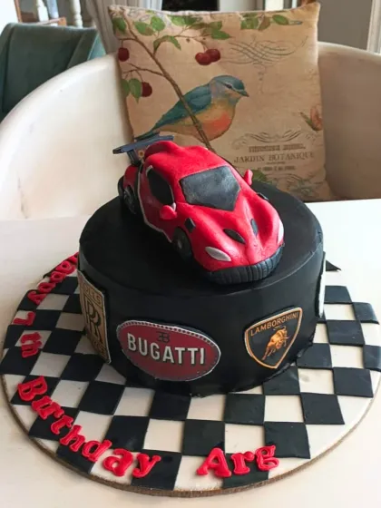 A high-octane supercar cake featuring a red Bugatti, checkered flag details, and luxury car brand logos.