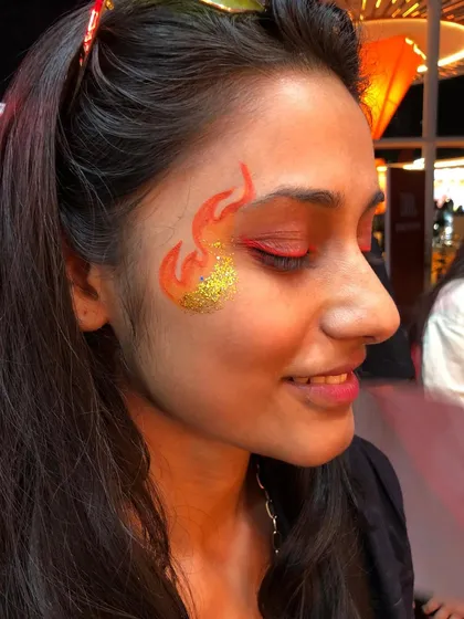 Bringing the heat with this fire-themed face art, complete with a sparkling gold glitter accent. This is a popular choice for music festivals and high-energy events.