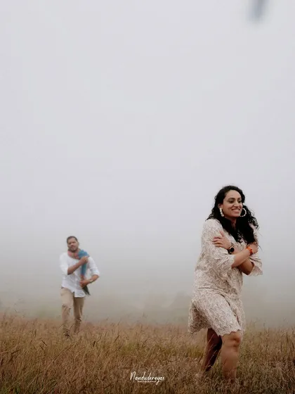 A candid shot of a couple in a misty field, capturing a genuine moment of joy and playfulness.