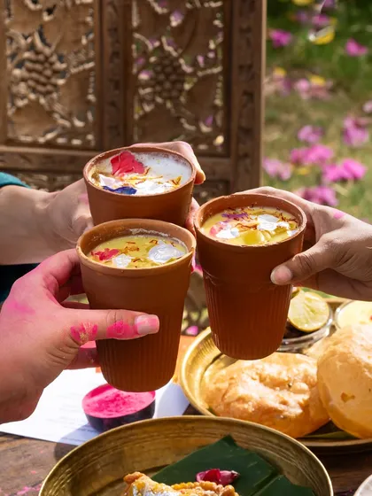 A toast with colorful Thandai during Holi celebrations. The colored hands and festive drinks capture the joyful spirit of the festival.