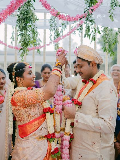 The bride and groom share a joyful moment during the Varmala ceremony. The overhead floral decor with hanging green amaranthus adds a touch of modern elegance to the traditional ritual.
