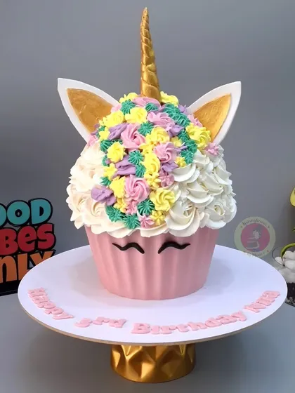 A giant cupcake cake for a 3rd birthday! This fun and whimsical design is covered in colorful buttercream rosettes and features a golden unicorn horn.