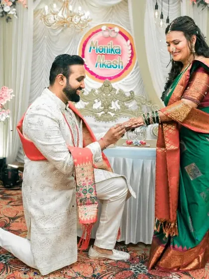 The groom-to-be gets down on one knee to place the ring on his fiancée's finger, a classic and heartwarming proposal moment during their engagement ceremony.